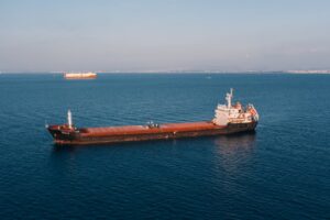 Aerial view of a cargo ship sailing in the open sea under clear skies, showcasing maritime transport.
